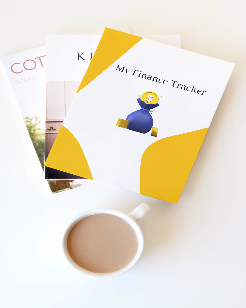 My Finance Tracker  with Blue money bag in the middle with yellow dollar coins on top and sides of the blue money bag. The document is sitting on top of two magazines.